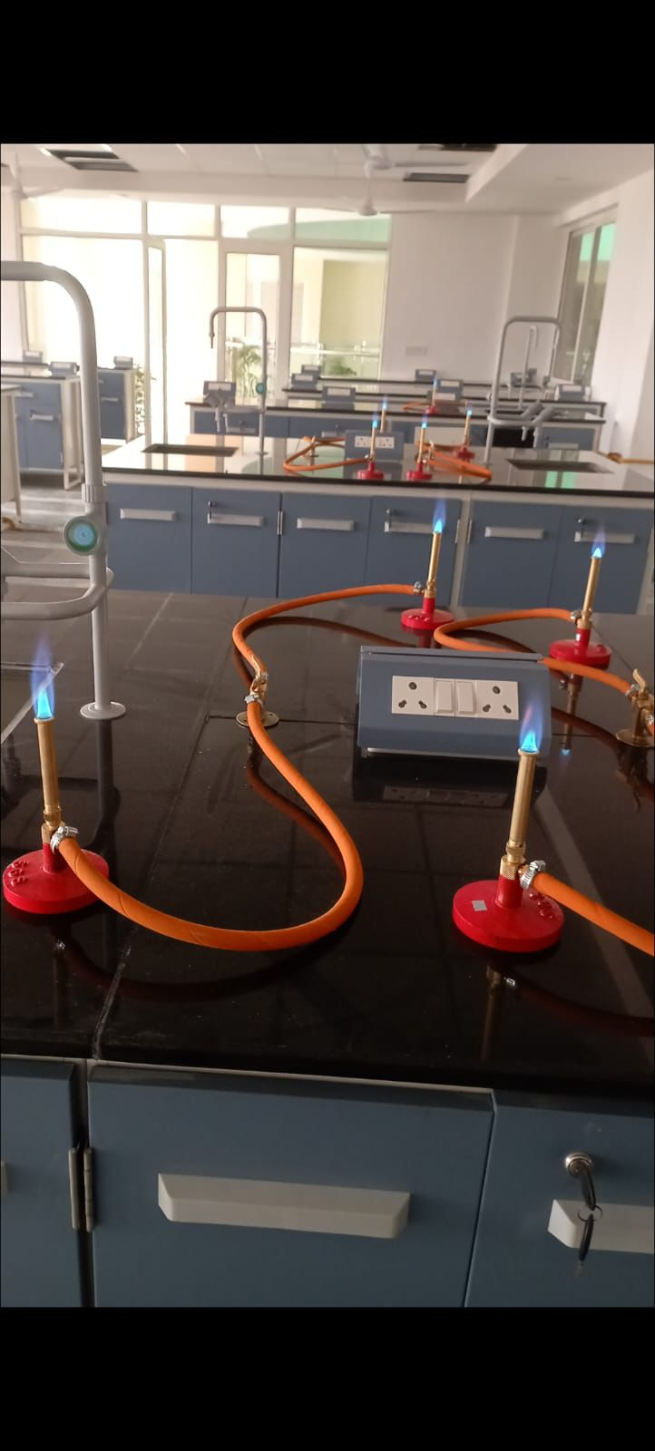 Lab gas supply with lit Bunsen burners on black bench tops